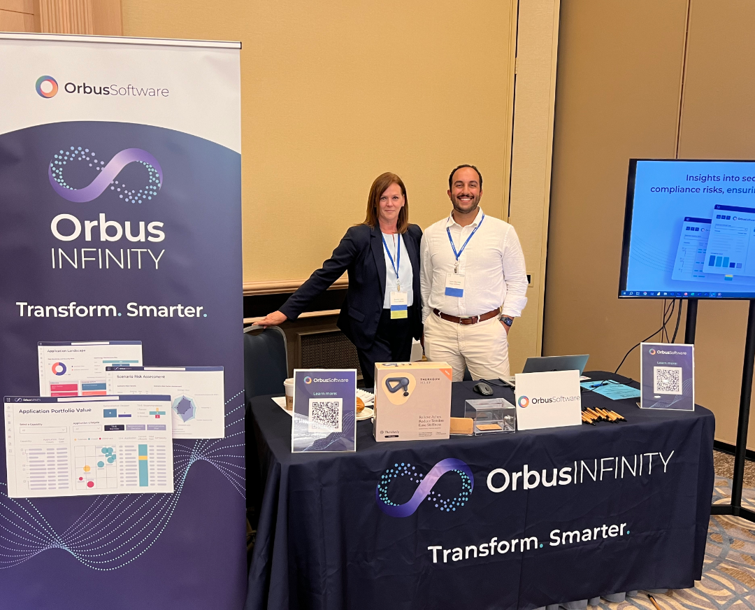 Two Orbus Software representatives, Brenda Cowie and Yazan Abutaleb, stand next to a display booth for Orbus Software at CAMP IT's 2024 Enterprise Architecture Conference.