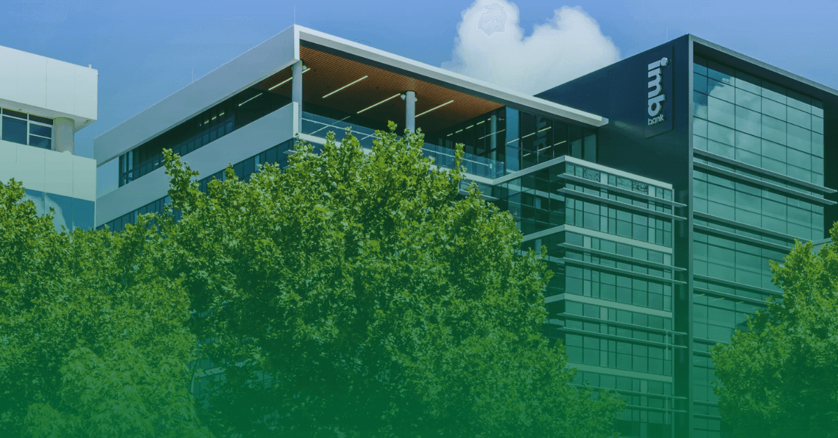 A modern office building of IMB Bank surrounded by lush green trees, showcasing the bank's commitment to sustainability and a clean, eco-friendly environment.